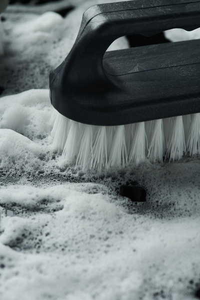 Close-up of a household iron brush with a black handle and white bristles in soap foam